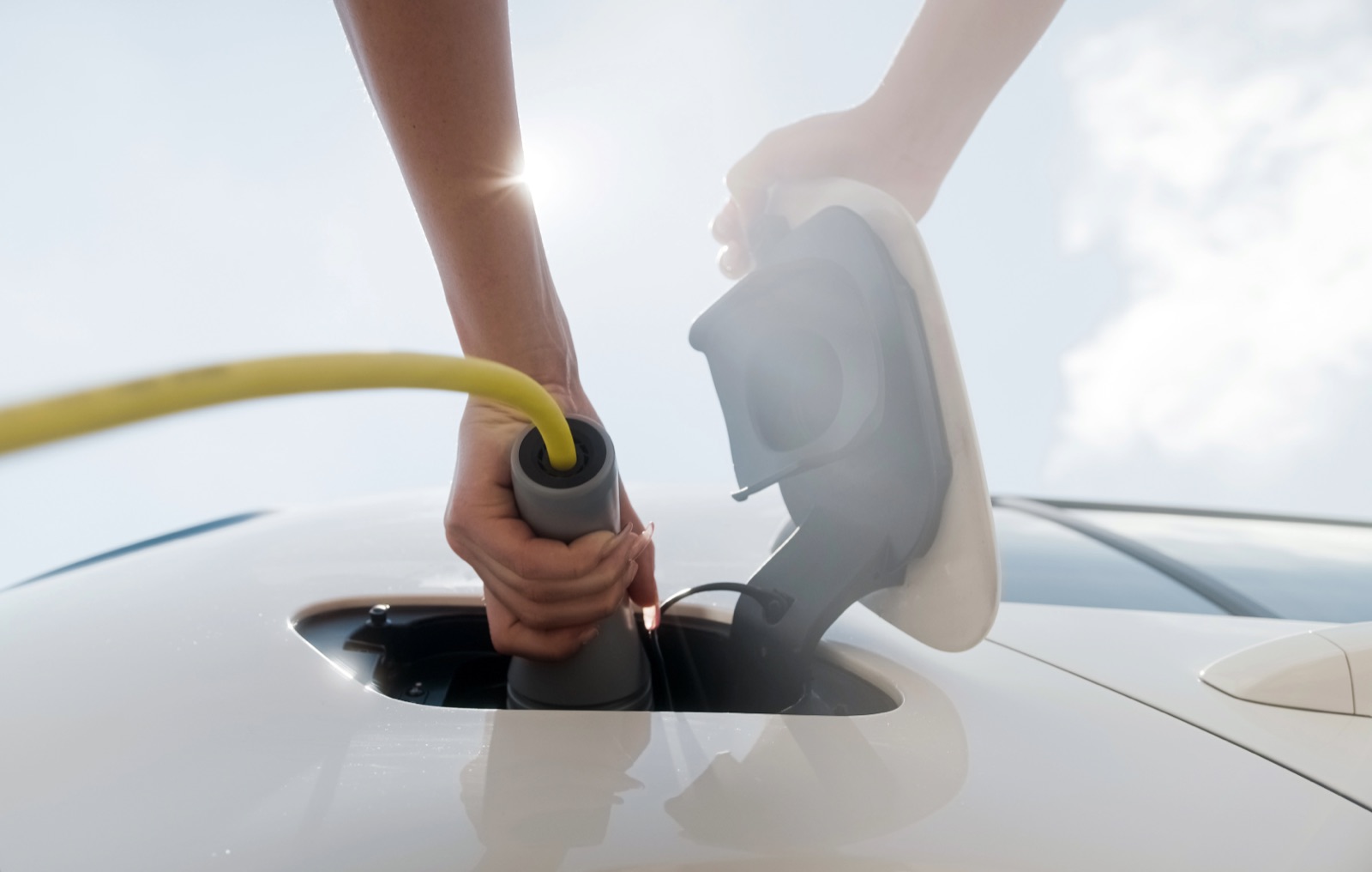 A driver plugging a charging connector into a white electric vehicle